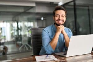 Man sitting in front of a laptop smiling because of Dental Crowns at Westlake Village Dental