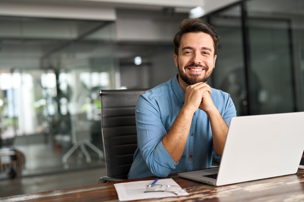 Man sitting in front of a laptop smiling because of Dental Crowns at Westlake Village Dental