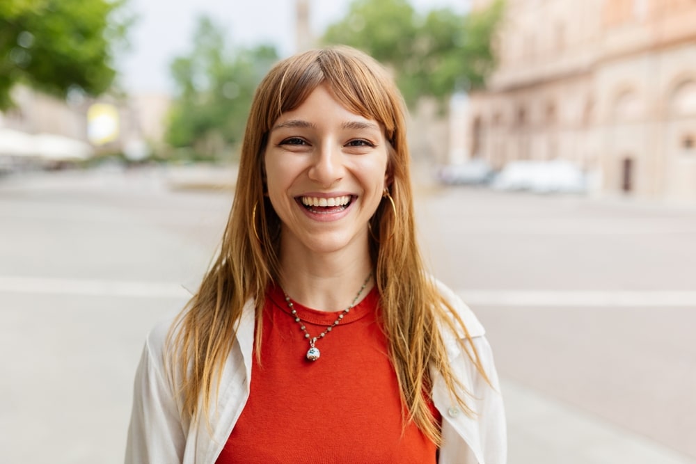 Female teenager with an orange shirt smiling because of Dental Implants at Westlake Village Dental