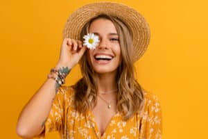 A smiling woman holding a flower while wearing a straw hat for Dental Services at Westlake Village Dental